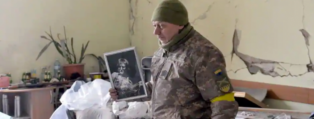 Un Ukrainien montre un portrait du chanteur britannique John Lennon, dans un appartement de Kharkiv détruit par les bombes, le 1er mars 2022. | SERGEY BOBOK / AFP