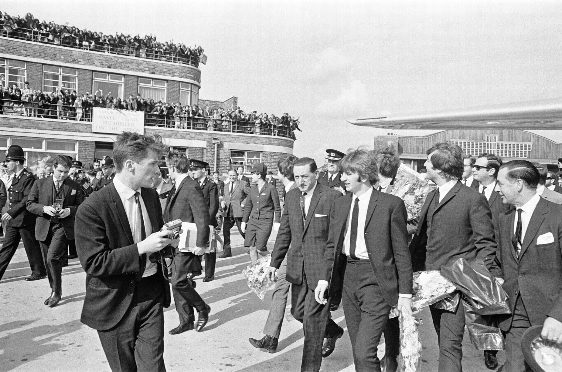 John Lennon, Ringo Starr et George Harrison photographiés ici quittant l'aéroport après leur vol vers Liverpool. Les fans et les photographes les saluent. juillet 1964  (Image : Mirrorpix)